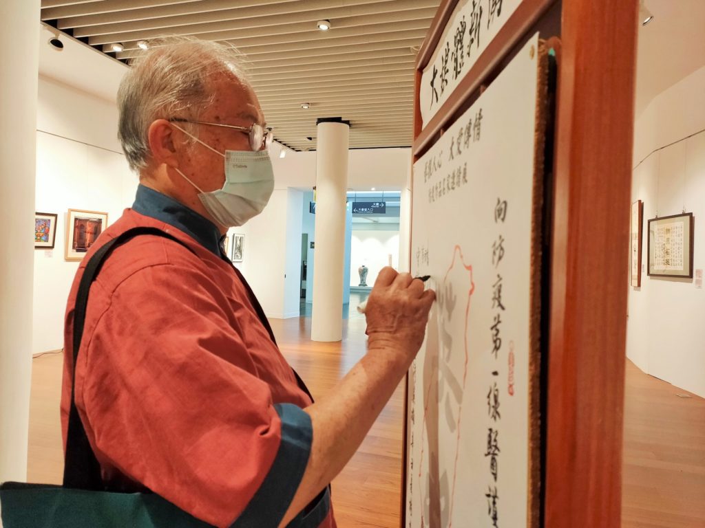 以篆體防疫文參展以鼓舞民心的知名書法家沈榮槐會長,在臺灣加油祈福板上簽名。(圖/詹美絨 攝)
