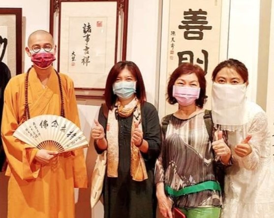 大慧法師(左一)與他的書畫老師信眾,在他的書體防疫作品「諸事吉祥」前留下史實見證。(圖/詹美絨 攝)