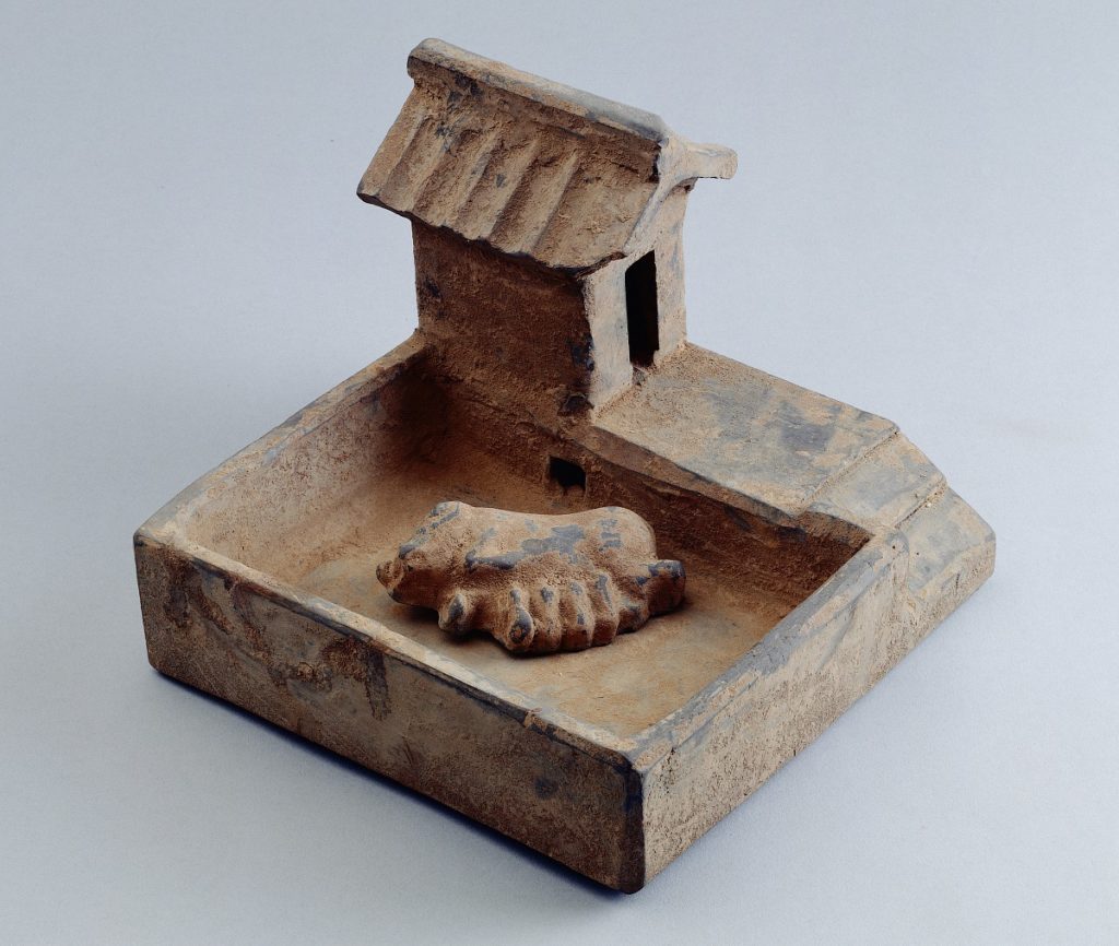 灰陶豬圈 漢 高14 長19 寬21 cm (史博館典藏陶器:77-00640) 「家」的字形演變中,上方的「宀」表示房子「宀」下有「豕」表示在家中下層養豬。此件帶廁豬圈,下方是豬圈,上方為人廁;人廁的下方鏤空與豬廁相連,以利人的排泄物直達豬圈,給豬提供食物。