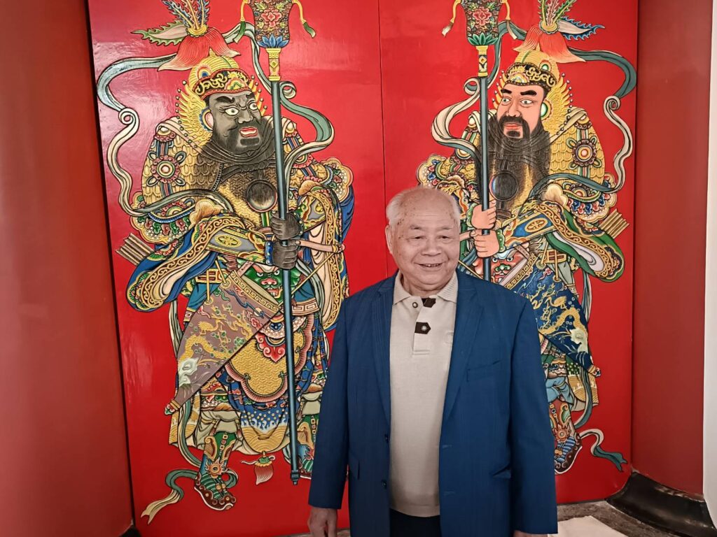 國寶級的彩繪工藝畫師莊武男,在史博館的大門門神作品前開心留影,神情愉快。(記者 辛澎祥/攝)