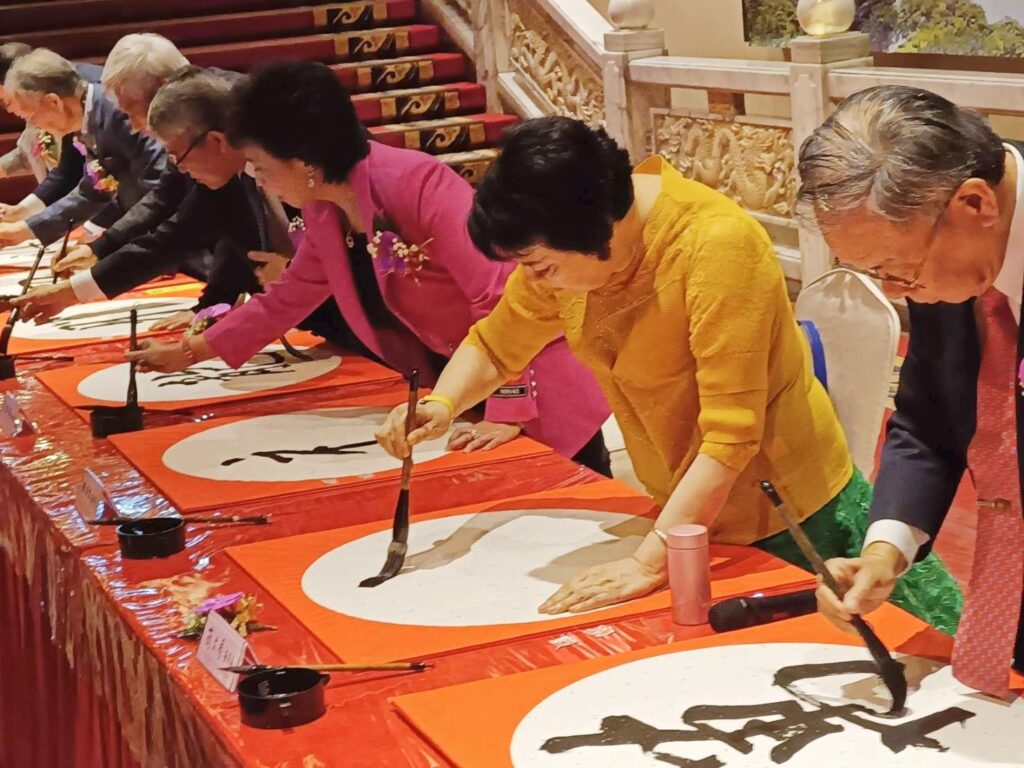 ▲圓山飯店的開筆揮毫活動，簡文秀（右二）也不遑多讓寫下祝福大字。圖右為中華書會會長張炳煌教授。（記者 辛澎祥/攝）