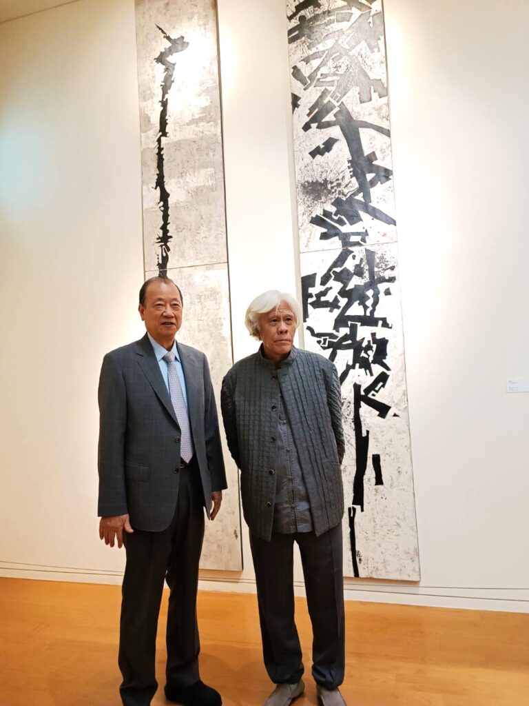王懷慶(右)為觀者介紹創作歷程,並與亞洲大學創辦人蔡長海於作品「連環棍」「鶴頭杖」前合影。(記者 陳安婷/攝)