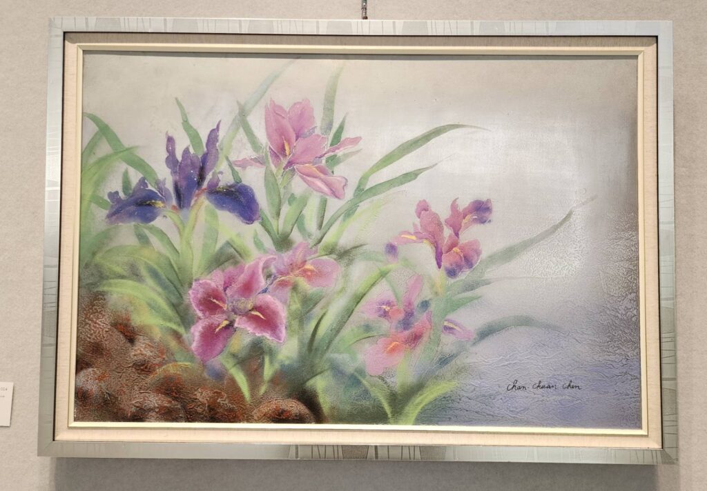 ▲台灣綠水畫會陳嬋娟理事長的展出作品「鳶尾花開」,別出心裁的以不鏽鋼板作為畫板,用去色法取代傳統的層層敷彩,構圖明亮且具生命力。(記者 辛澎祥/攝)