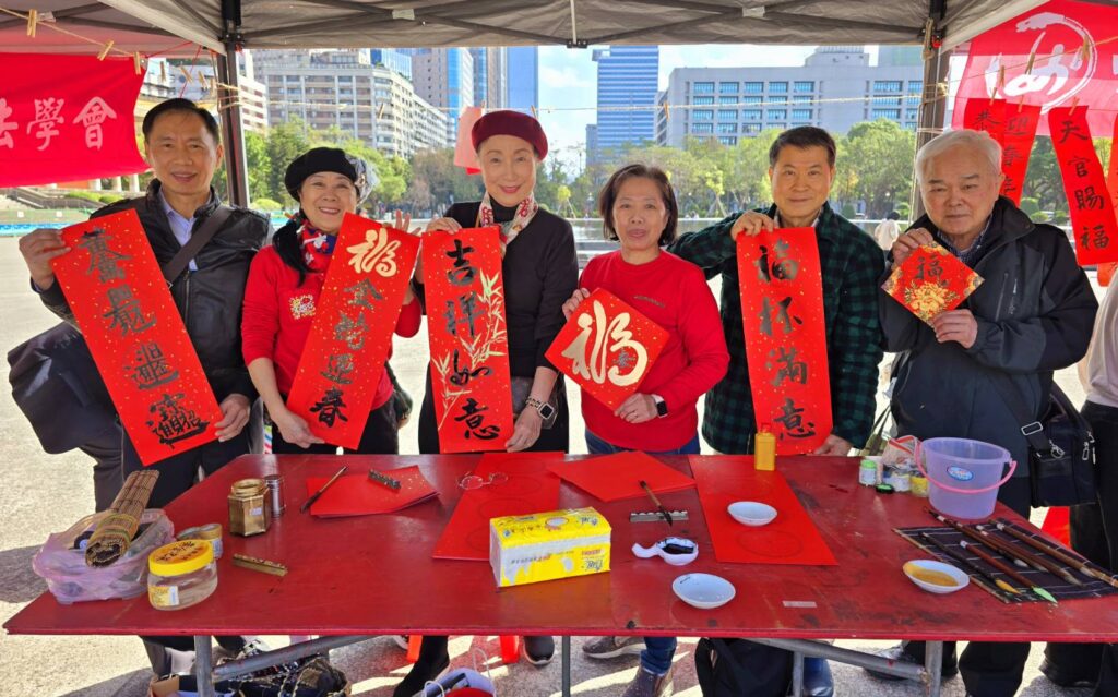 中華娛樂文創產業發展協會揮毫寫春聯的老師，左起程銘洲、陳月里、何慶珍、詹美絨、廖仁彬與李其融，開心的拿著春聯作品合影。（記者 陳安婷/攝）