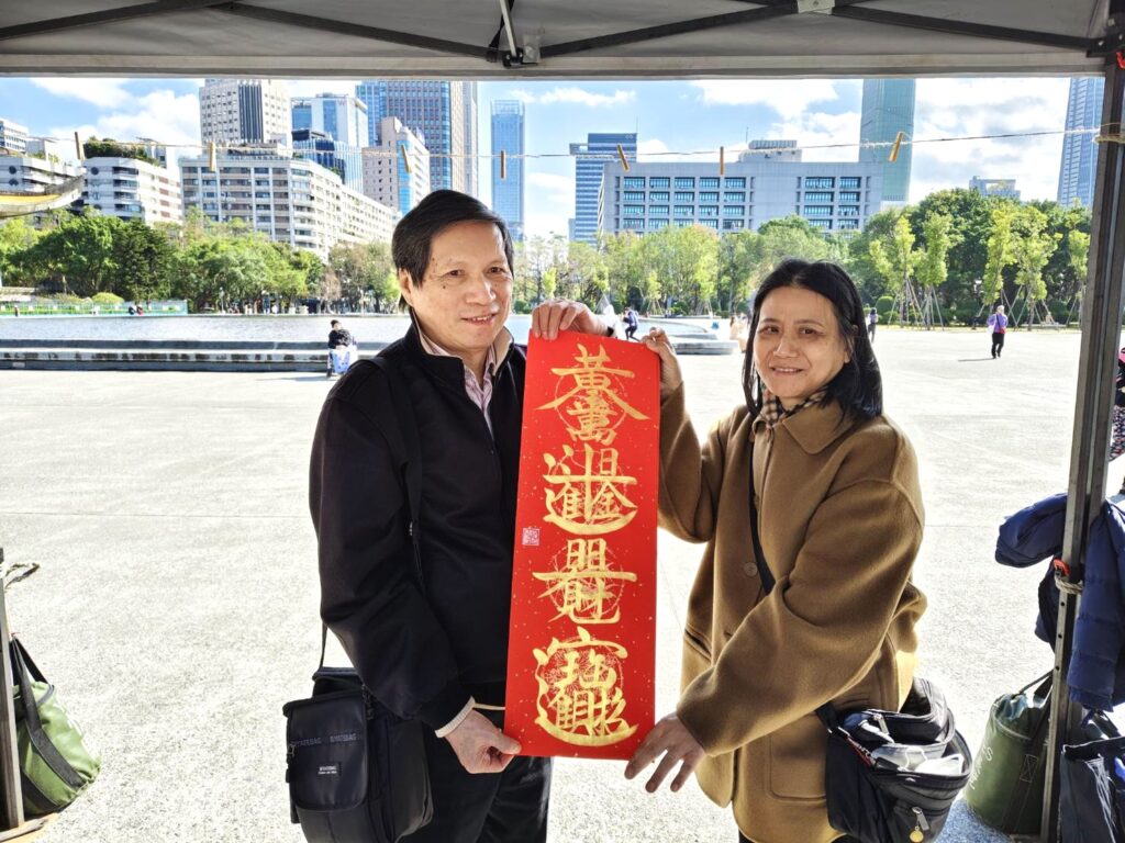 書法家游錫賢(左)老師的春聯別出心裁，民眾拿到開心合影留念。（記者 陳安婷/攝）