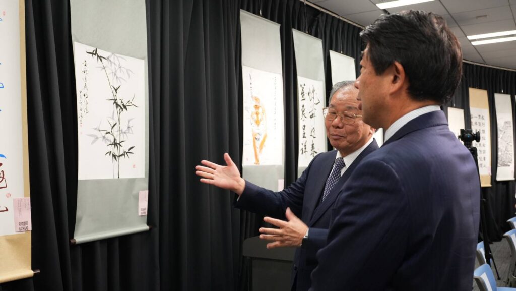 ▲臺灣知名書法家張炳煌（左）在東京書畫展展場向日本政界人士做作品的導覽與介紹。（圖/文化部 提供）