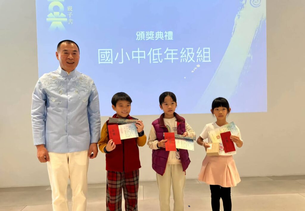 ▲大愛光老師周瑞宏（左）頒發優勝作品獎給國小中低年組得獎者，並與得獎者開心合影留念。（記者 辛澎祥/攝）