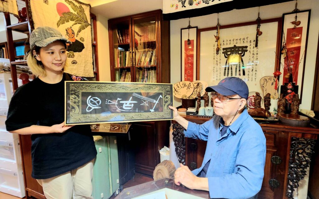 ▲施春茂老師以甲骨文書體撰寫「我在故我思」的創作思想，藉此遵循此藝術信念做自我要求，期許成長。左為施春茂老師助理崔毅。（記者 辛澎祥/攝）