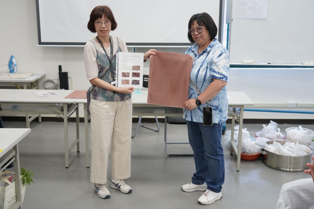 纖博館簡惠華主任(左)和工作營講師孫翠蘭展示學員合作完成的「大里001色」樣布。（圖/纖維工藝博物館提供）