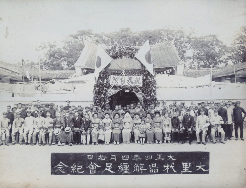 臺中州廳長官私人寫真帖（二）55 大里杙街在今臺中市東南部，1915年4月該街放足者已達1,200人，未放足者僅餘152人。大里杙解纏足會乃於4月10日上午集合已放足會員300人，在大里杙區役場前舉行解纏足祝賀會，會後舉行餐會，並贈送出席會員木屐一雙。牌坊上寫著「祝我自然」四字。（圖/國家攝影文化中心提供）