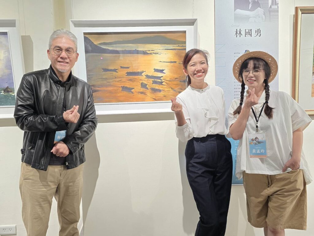 ▲參展藝術家林國勇(左)與參展創作人在展場開心交流互動,場面輕鬆自在。後為林國勇所展出之水彩作品。(記者 詹佳綺/攝)