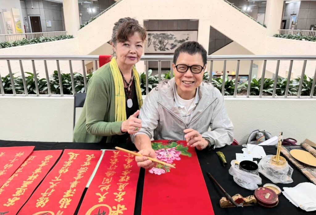 ▲來自桃園的水墨畫家梁瑞琴（左）與台北參展藝術家林加添相見歡，寫春聯時興致高昂。（記者 詹佳綺/攝）