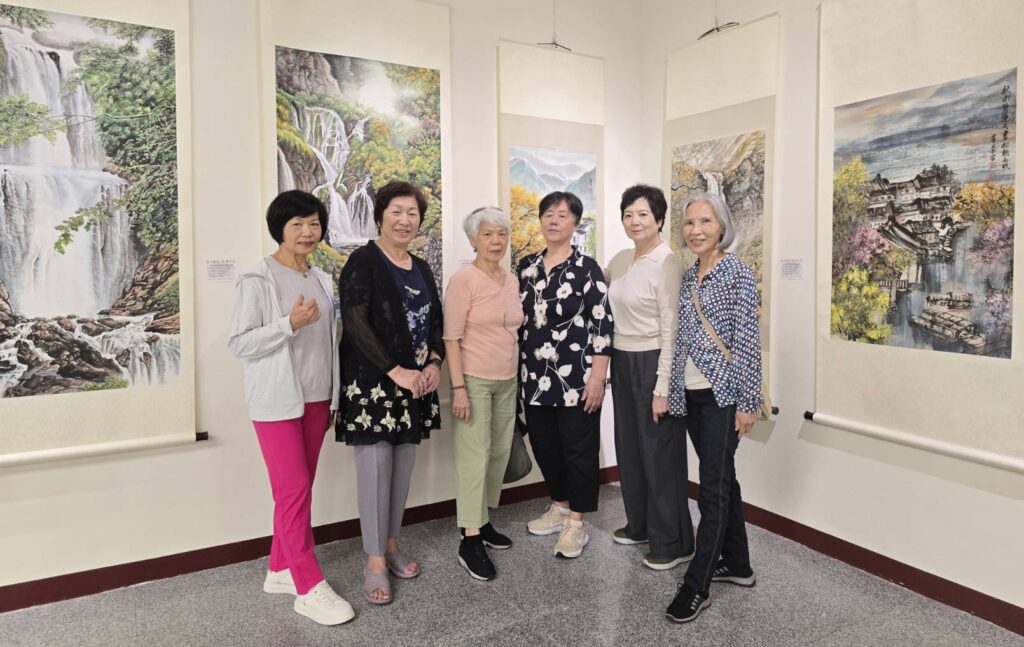 ▲參展藝術家楊麗玲(左二)與她的畫友們在水墨作品前留影,投身在山海景物的創作中,頓時備顯開心自在。(記者 詹佳綺/攝)