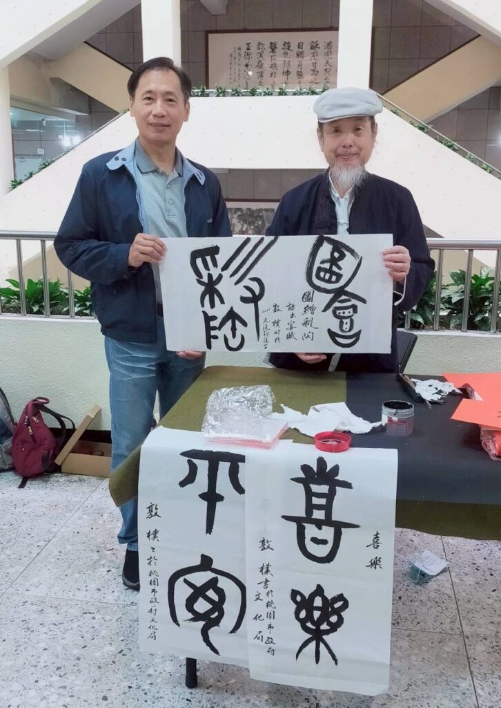 ▲書法老師程銘洲（左）與陳文樹，現場揮毫書寫金文作品，觀賞上饒富趣味。（記者 詹佳綺/攝）