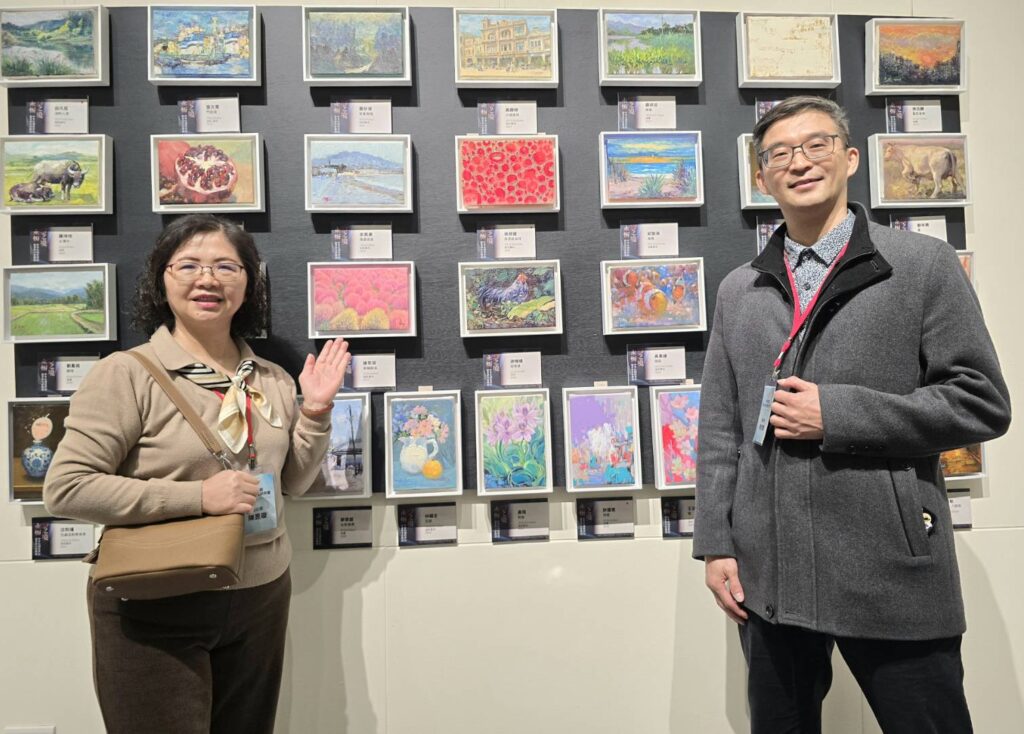 ▲中華民國跨世紀油畫研究會理事長徐欣健（右）與秘書長陳昱璇在參展藝術家別緻的小品畫作展板前合影及推薦優質藝術家作品。（記者 詹佳綺/攝）