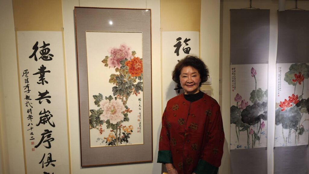 ▲李中華館長在展出的父親李超哉大師的書法及她的水墨畫作品前合影，對父親的書藝功力認為自己有很大的學習與體悟。（記者 辛澎祥/攝）