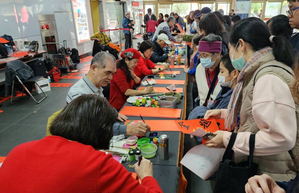▲中華娛樂文創產業發展協會的12位書畫老師，專注於寫春聯的情形，民眾爭向索取春聯，場面相當熱烈。（圖/大媒體新聞網 提供）