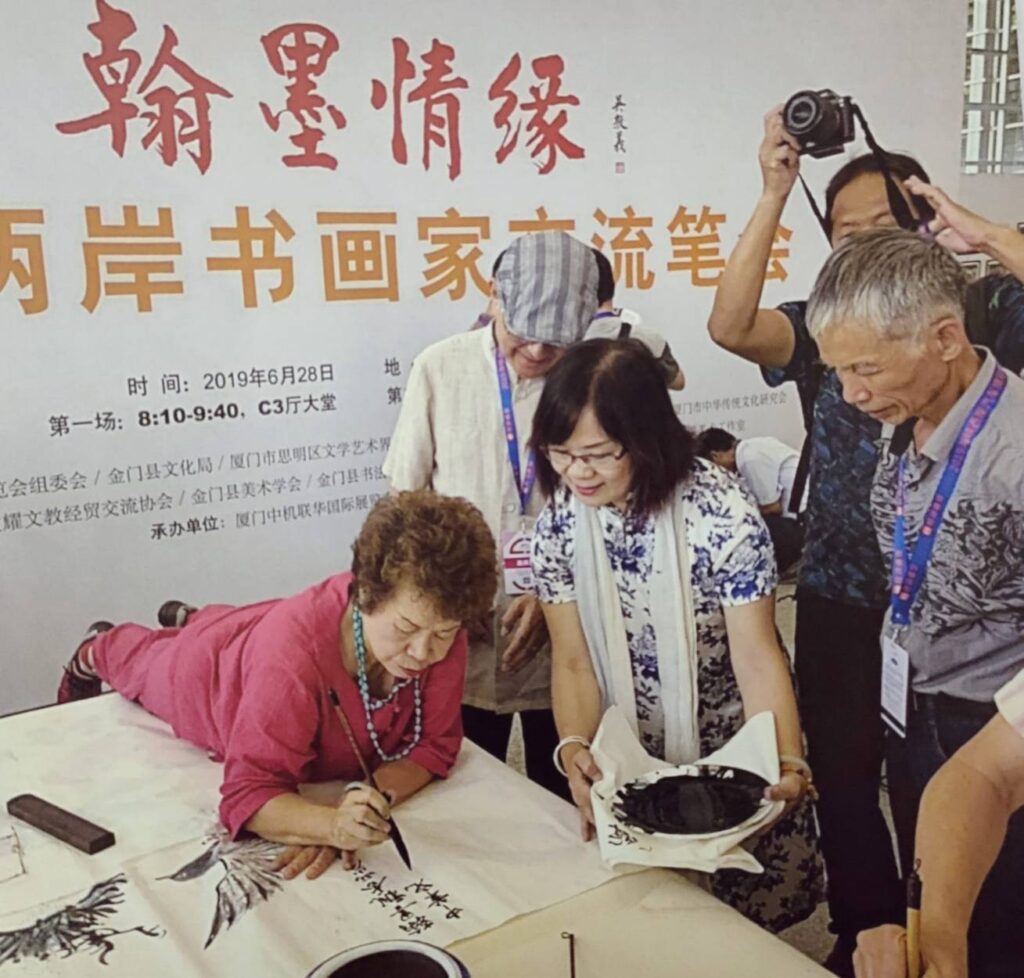 ▲數十年來的兩岸文化交流活動中，有時後都能看到呂玉環老師（左）趴在桌上現場揮毫的盛況。（圖/本社資料照）