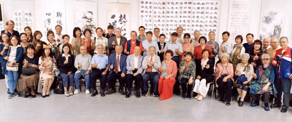 ▲不管大小展，不論個聯展，只要合影場面，都能看到呂玉環老師（前排右六）鮮豔色彩服飾所成為現場的焦點。（記者 詹佳綺/攝）