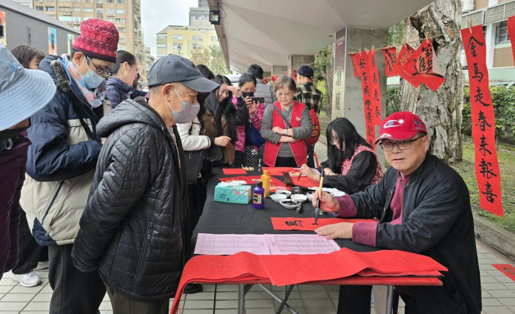 ▲澹廬書會理事長林俊光（右）與女兒林奕辰（右二）聯袂寫春聯給等待索取的民眾，成為現場矚目焦點。（記者 詹佳綺/攝）