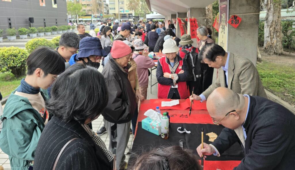 ▲中國書法學會理事長陳銘鏡（右二）與秘書長沈致中（右一）專注寫春聯引起民眾熱切圍觀。（記者 詹佳綺/攝）