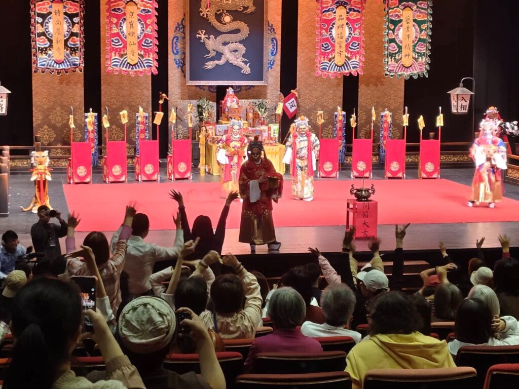 財神爺台上撒糖,台下觀眾舉手搶著要,熱鬧又逗趣。(圖/國光劇團提供)