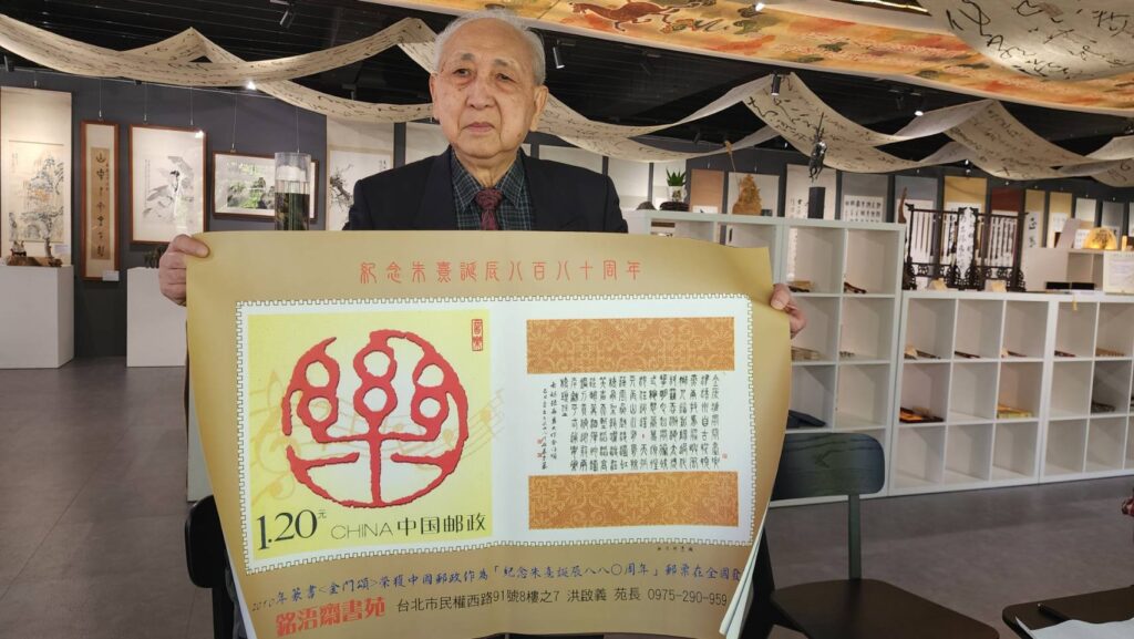 ▲洪啟義老師展示他在16年前以書寫篆體作品「金門頌」，獲得北京郵政總局發行郵票的殊榮，備受矚目。（記者 辛澎祥/攝）