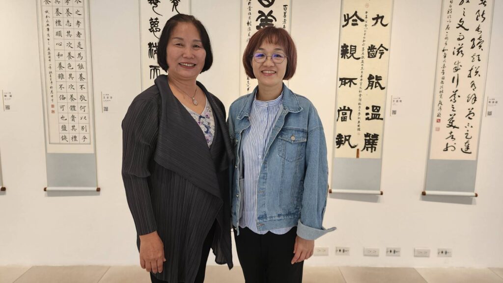 ▲和氣大愛文教基金會董事長段傳芬（左）與資深員工李依璇在展場得獎者書法作品前受訪，神情相當愉快。（記者 辛澎祥/攝）