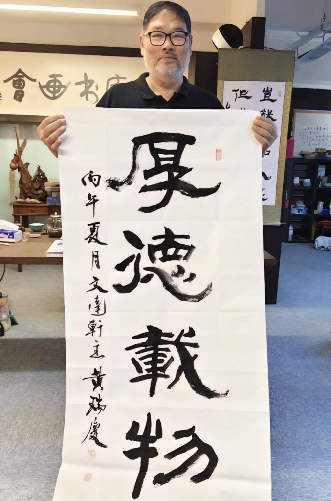 ▲馬來西亞書藝總會黃瑞慶會長揮毫書寫「厚德載物」文句,筆觸充滿圓融大器,聚焦眼界。(記者 辛澎祥/攝)
